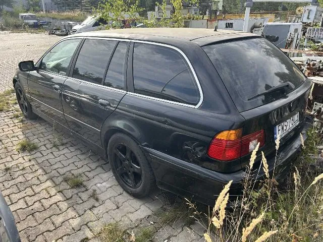 Czarny samochód osobowy typu kombi zaparkowany na kostce brukowej. Pojazd jest widoczny z tyłu i z boku, ma przyciemniane szyby i czarne felgi. Na tylnej klapie widoczna jest tablica rejestracyjna o numerze FWS 73CJ. W tle widać inne pojazdy oraz elementy infrastruktury przemysłowej.