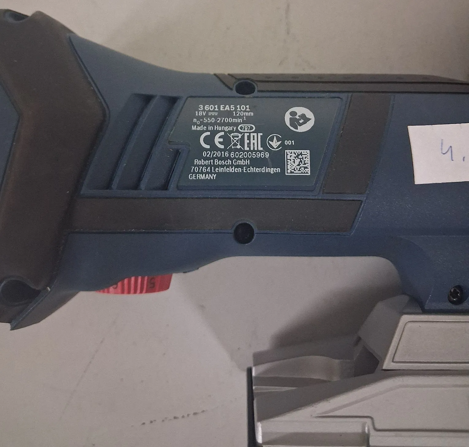 Zbliżenie na niebieską obudowę elektronarzędzia z naklejoną tabliczką znamionową. Na tabliczce znajduje się tekst: '3 601 EA5 101', '18V ⎓ 1,20mm', 'n0 550-2700min-1', 'Made in Hungary 797', znaki CE i EAC, numer '001', '02/2016 602005969', 'Robert Bosch GmbH', '70764 Leinfelden-Echterdingen', 'GERMANY' oraz kod QR. Po prawej stronie widoczna jest biała naklejka z odręcznym zapisem '4,'.