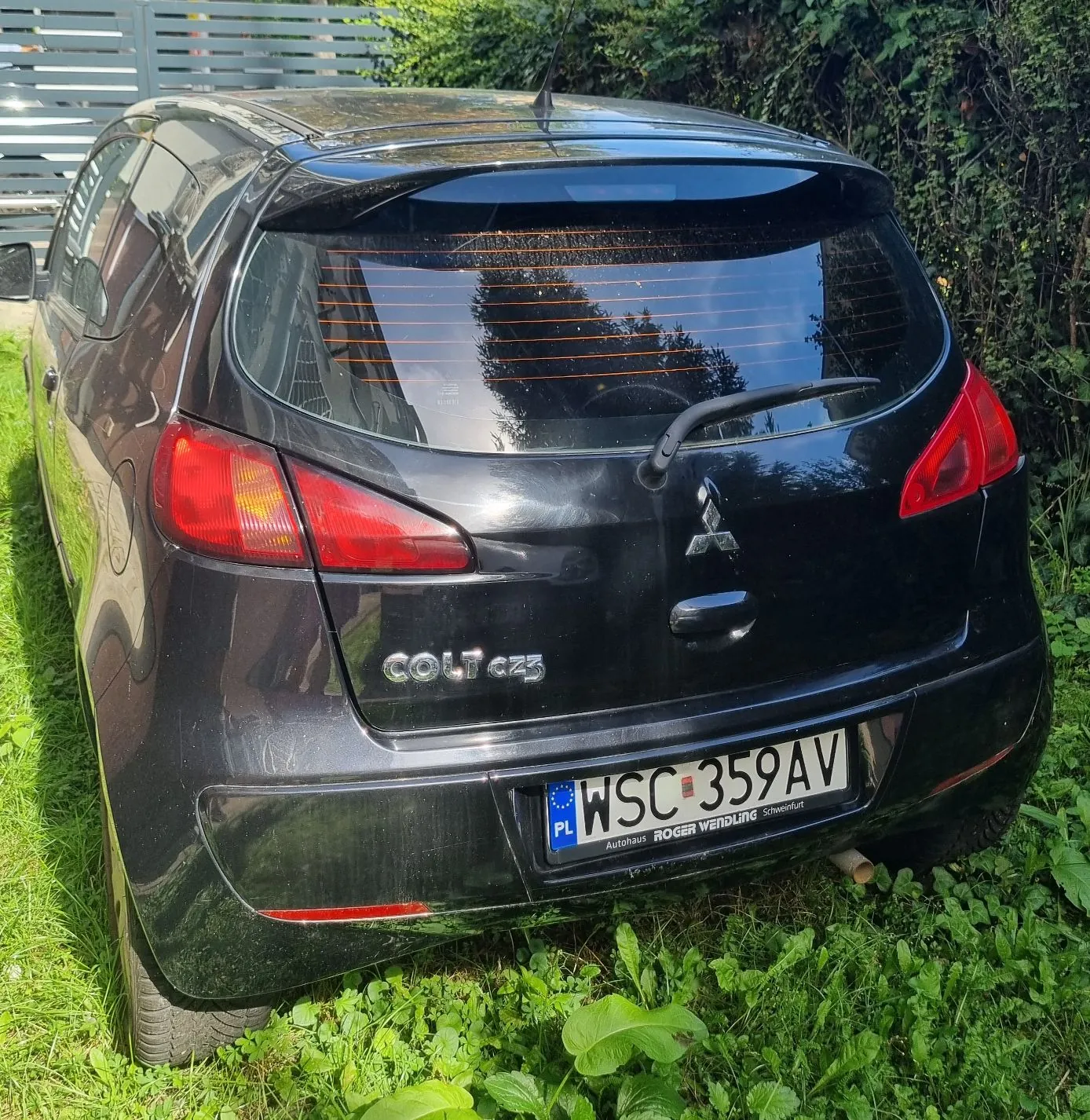 Tylny widok czarnego samochodu marki Mitsubishi Colt CZ3 zaparkowanego na trawie. Na klapie bagażnika widoczne jest logo Mitsubishi oraz napis COLT CZ3. Samochód posiada polską tablicę rejestracyjną o numerze WSC 359AV, a pod nią znajduje się napis Autohaus ROGER WENDLING Schweinfurt.