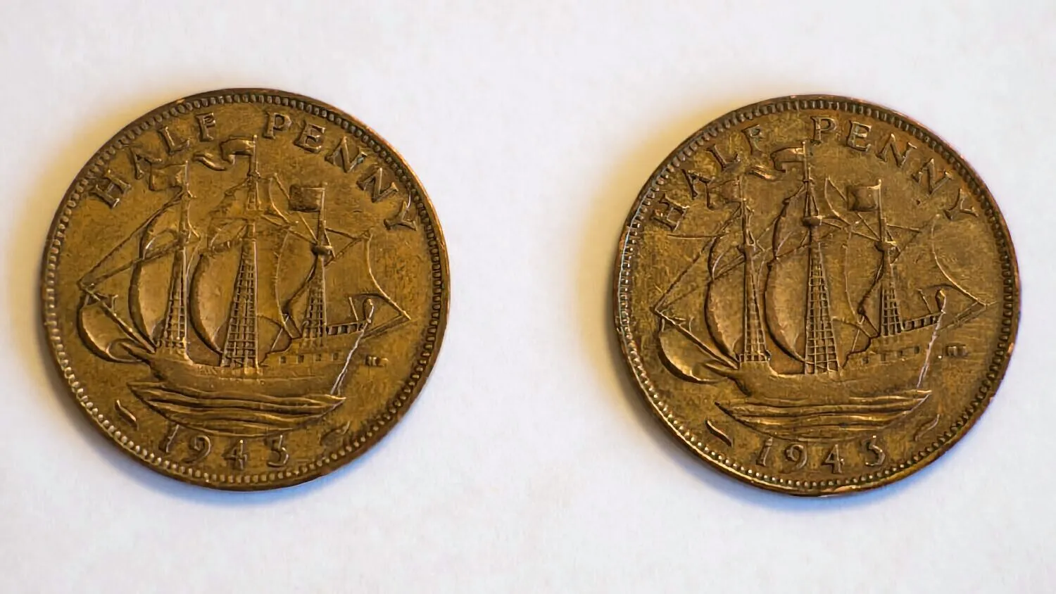 Dwie identyczne, miedziane monety o nominale Half Penny z roku 1943, ułożone obok siebie na białym tle. Na każdej z monet widnieje wizerunek żaglowca oraz napisy: 'HALF PENNY' u góry i '1943' na dole.