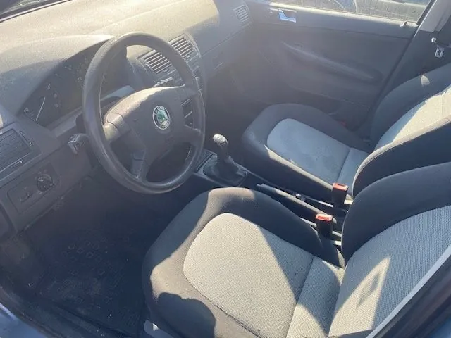 Wnętrze samochodu z widocznym kierownicą z logo, deską rozdzielczą, dźwignią zmiany biegów, czarno-szarymi siedzeniami oraz panelami drzwiowymi. Światło słoneczne wpada przez okna, oświetlając wnętrze.