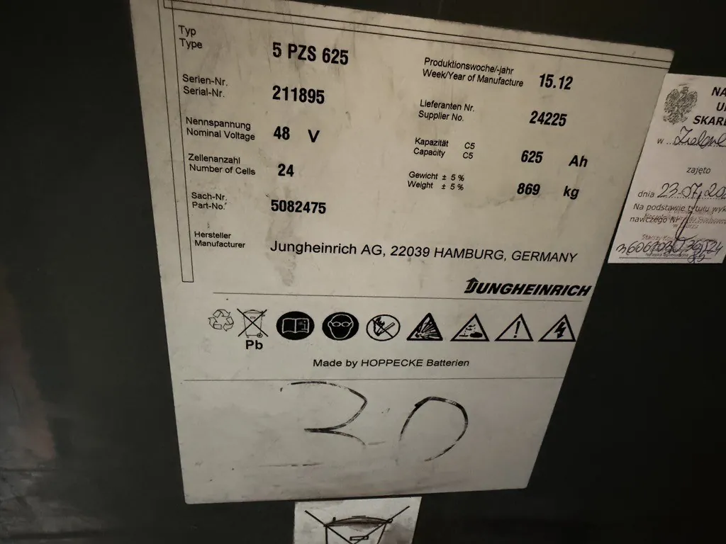 Zdjęcie tabliczki znamionowej urządzenia marki Jungheinrich. Tabliczka zawiera następujące dane techniczne: Typ: 5 PZS 625, Produkcyjne tydzień/rok: 15.12, Numer seryjny: 211895, Numer dostawcy: 24225, Napięcie znamionowe: 48 V, Pojemność C5: 625 Ah, Liczba ogniw: 24, Waga: 869 kg, Numer części: 5082475. Producentem jest Jungheinrich AG, 22039 Hamburg, Niemcy. Na dole znajduje się napis 'Made by HOPPECKE Batterien' oraz zestaw piktogramów ostrzegawczych i instrukcyjnych. Poniżej tabliczki widnieje odręczny napis '30'. Po prawej stronie znajduje się fragment białej naklejki z odręcznymi notatkami w języku polskim.
