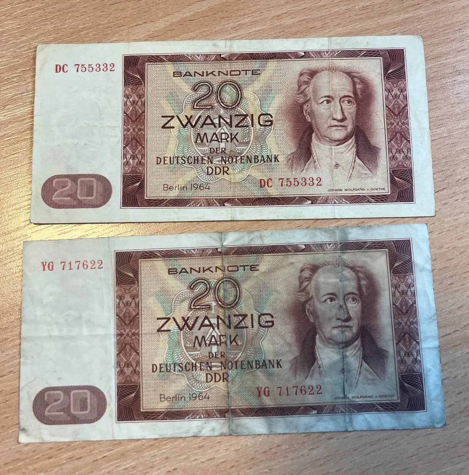 Dwa banknoty o nominale 20 marek z Niemieckiej Republiki Demokratycznej (DDR) z 1964 roku, ułożone jeden nad drugim na drewnianym blacie. Na każdym banknocie widnieje portret Johanna Wolfganga von Goethego, napis '20 ZWANZIG MARK DER DEUTSCHEN NOTENBANK DDR' oraz data 'Berlin 1964'. Górny banknot ma numer seryjny DC 755332, a dolny YG 717622.