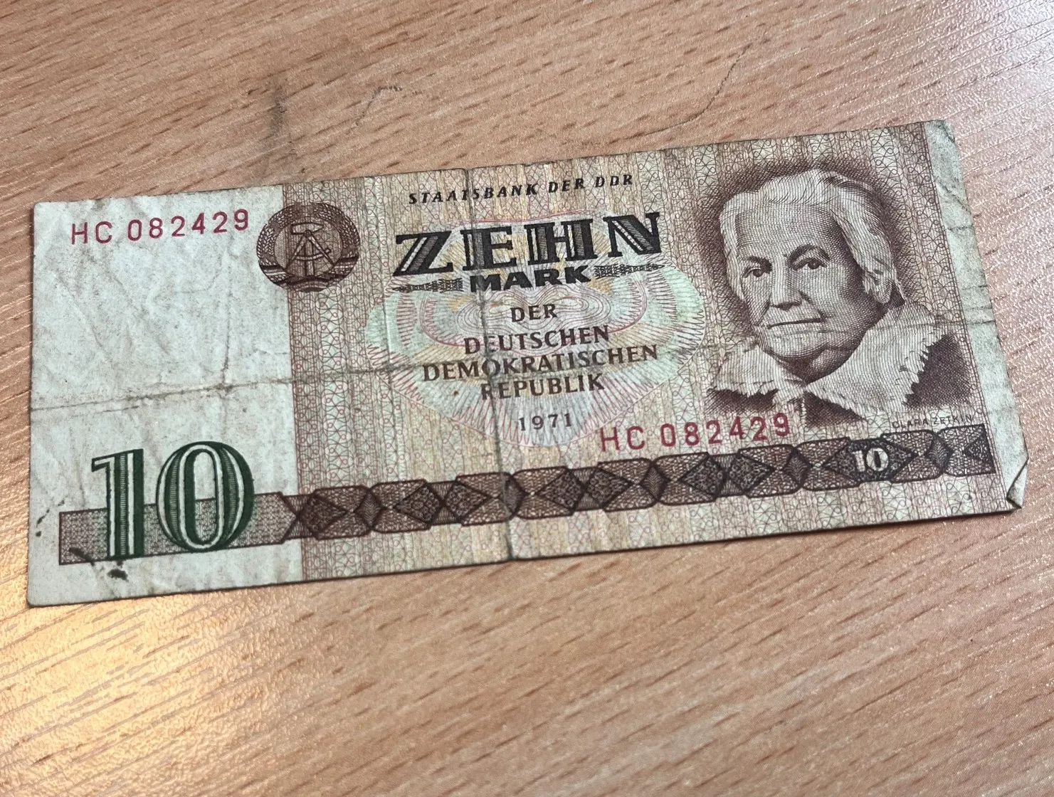 Banknot o nominale 10 marek z Niemieckiej Republiki Demokratycznej (NRD) z 1971 roku. Na banknocie widnieje portret mężczyzny, napis 'STAATSBANK DER DDR', 'ZEHN MARK DER DEUTSCHEN DEMOKRATISCHEN REPUBLIK' oraz numer seryjny 'HC 082429'. W lewym dolnym rogu znajduje się duża cyfra '10'. Banknot leży na drewnianej powierzchni.