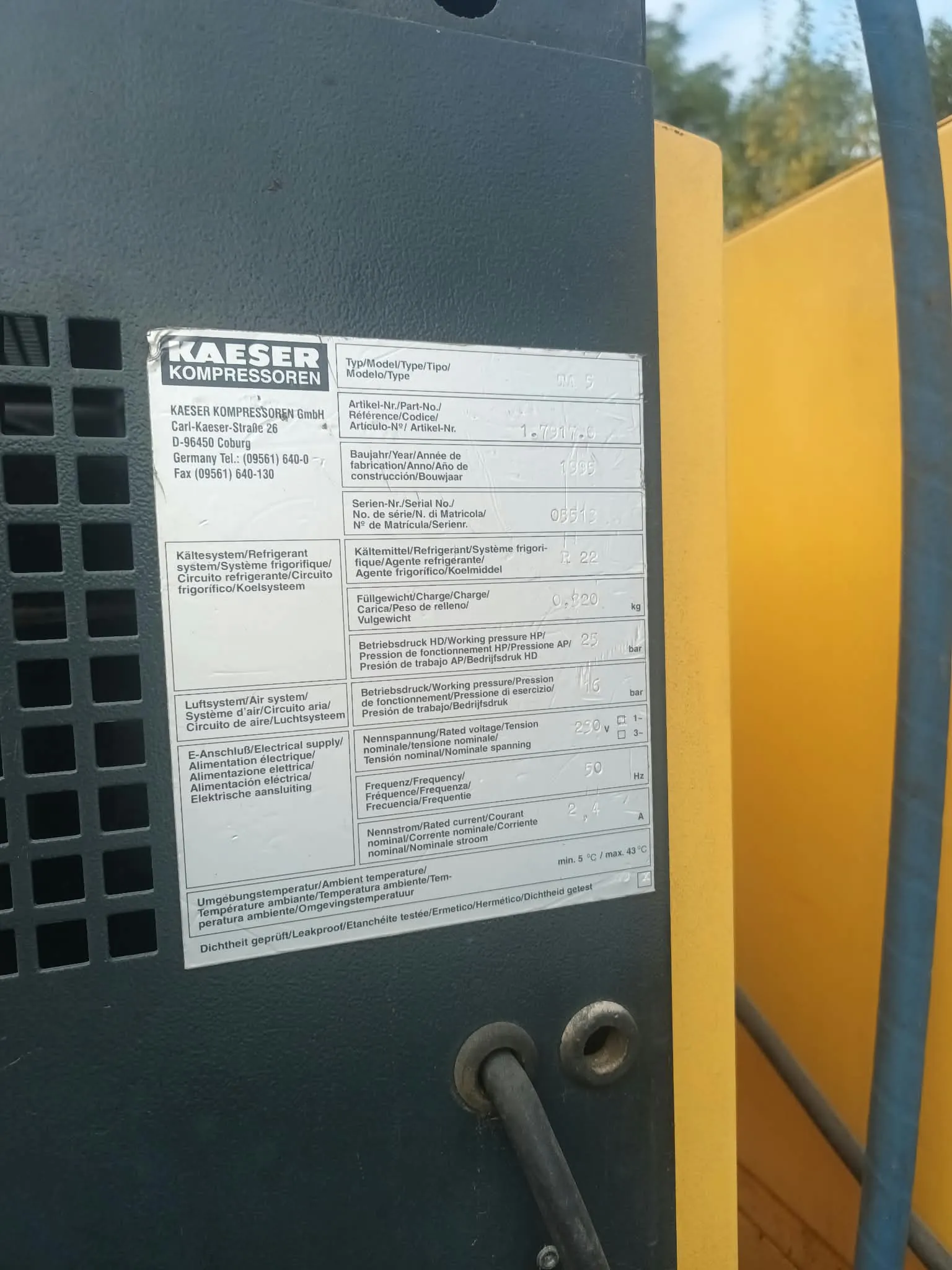Zdjęcie tabliczki znamionowej urządzenia firmy KAESER KOMPRESSOREN. Tabliczka jest srebrna z czarnymi napisami i polami do wpisania danych. Zawiera informacje techniczne w wielu językach, takie jak: adres producenta (Carl-Kaeser-Straße 26, D-96450 Coburg), numer artykułu, rok budowy, numer seryjny, rodzaj czynnika chłodniczego, ilość napełnienia, ciśnienie robocze, napięcie zasilania (230 V), częstotliwość (50 Hz) oraz prąd znamionowy. W dolnej części widnieje informacja o temperaturze otoczenia: min. 5 °C / max. 43 °C.
