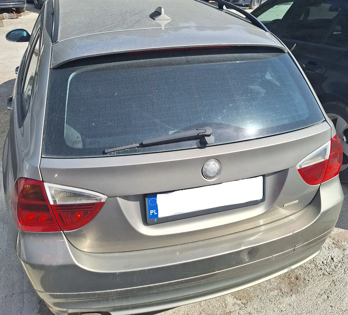 Tylny widok brązowego samochodu osobowego. Widoczna jest tylna szyba z wycieraczką, logo marki na klapie bagażnika oraz tablica rejestracyjna z oznaczeniem PL. Samochód jest zakurzony.