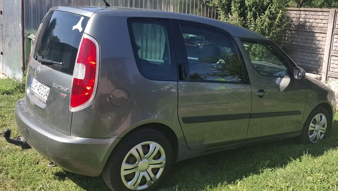 Szary samochód osobowy typu hatchback zaparkowany na trawie. Widoczny jest tył i prawy bok pojazdu. Samochód posiada tablicę rejestracyjną o numerze LOP 45334 oraz napis 'Astra' na klapie bagażnika. W tylnej szybie znajduje się biała naklejka w kształcie litery Y.