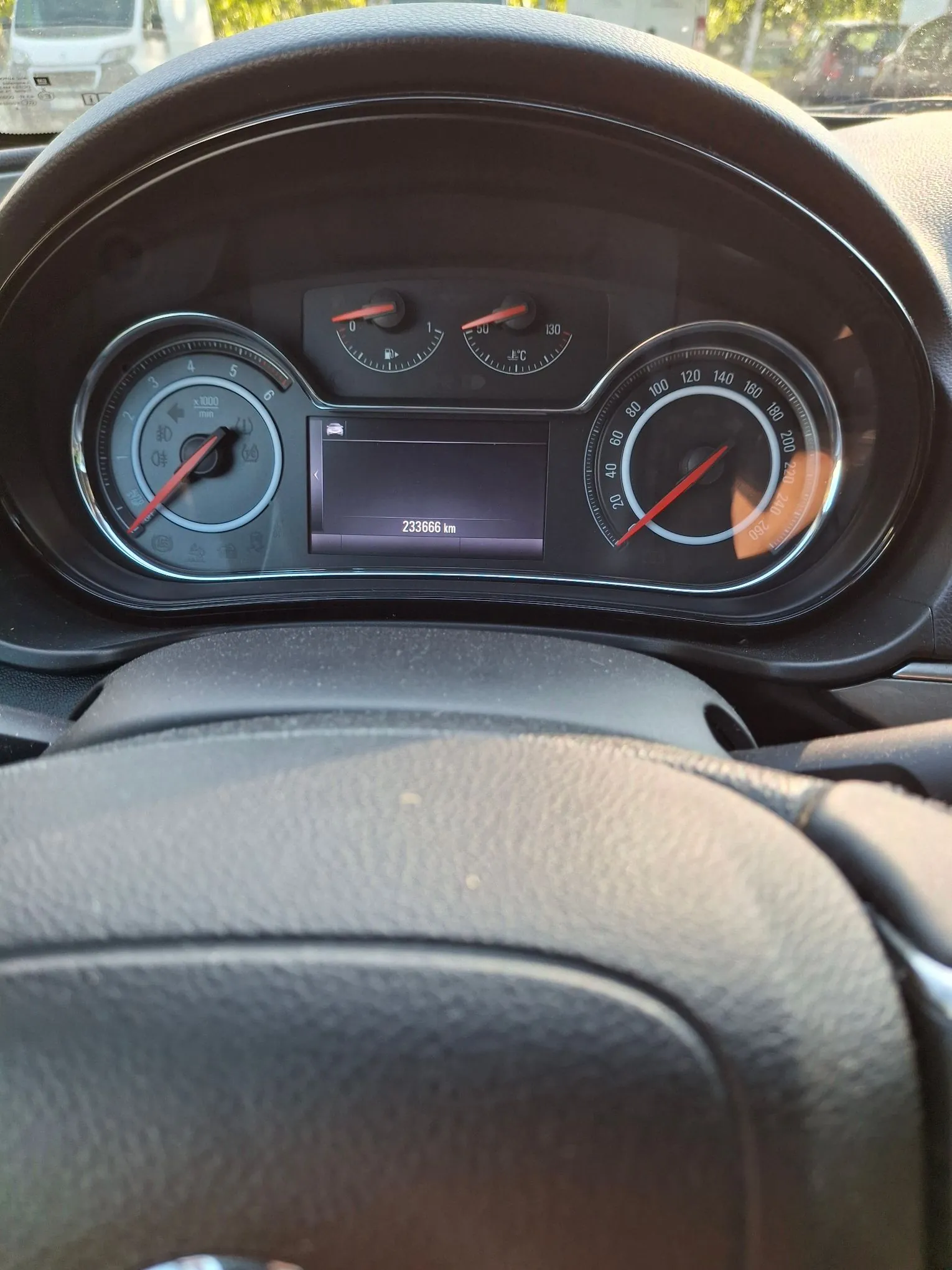 Zdjęcie z perspektywy kierowcy przedstawiające deskę rozdzielczą samochodu. Widoczne są dwa duże analogowe wskaźniki: po lewej obrotomierz, po prawej prędkościomierz. Nad nimi znajdują się mniejsze wskaźniki temperatury cieczy chłodzącej oraz poziomu paliwa. W centralnej części znajduje się cyfrowy wyświetlacz z napisem '233666 km'. Na pierwszym planie widoczny jest fragment górnej części kierownicy.