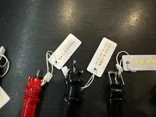 Trzy kluczniki: czerwony, czarny i czarny, każdy z białą etykietą zawieszoną na sznurku, ułożone na ciemnej powierzchni. Etykiety zawierają nieczytelny tekst.