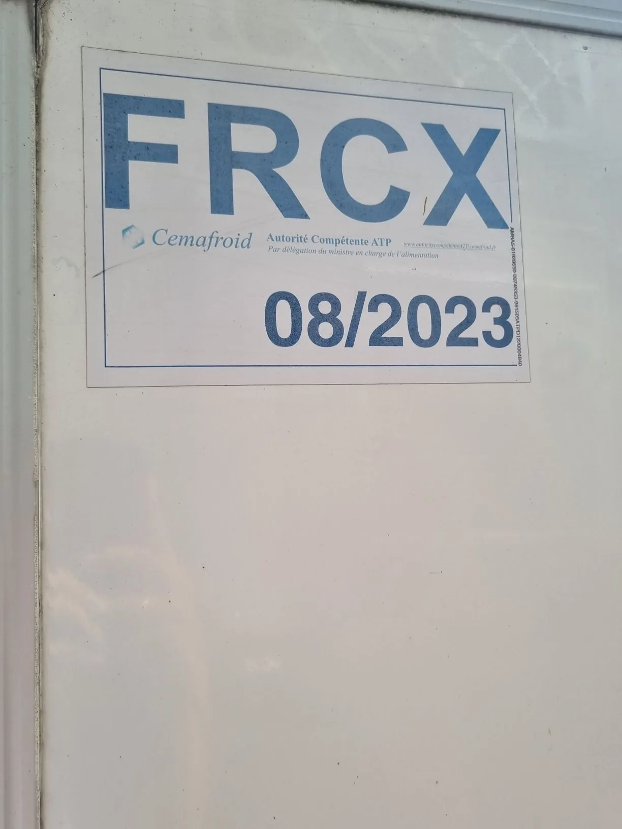 Biała powierzchnia z naklejoną prostokątną etykietą. Na górze etykiety znajduje się duży, niebieski napis „FRCX”. Poniżej widnieje logo i nazwa „Cemafroid” oraz tekst w języku francuskim: „Autorité Compétente ATP Par délégation du ministre en charge de l'alimentation” oraz adres strony internetowej. Na dole etykiety znajduje się duży, niebieski napis „08/2023”.
