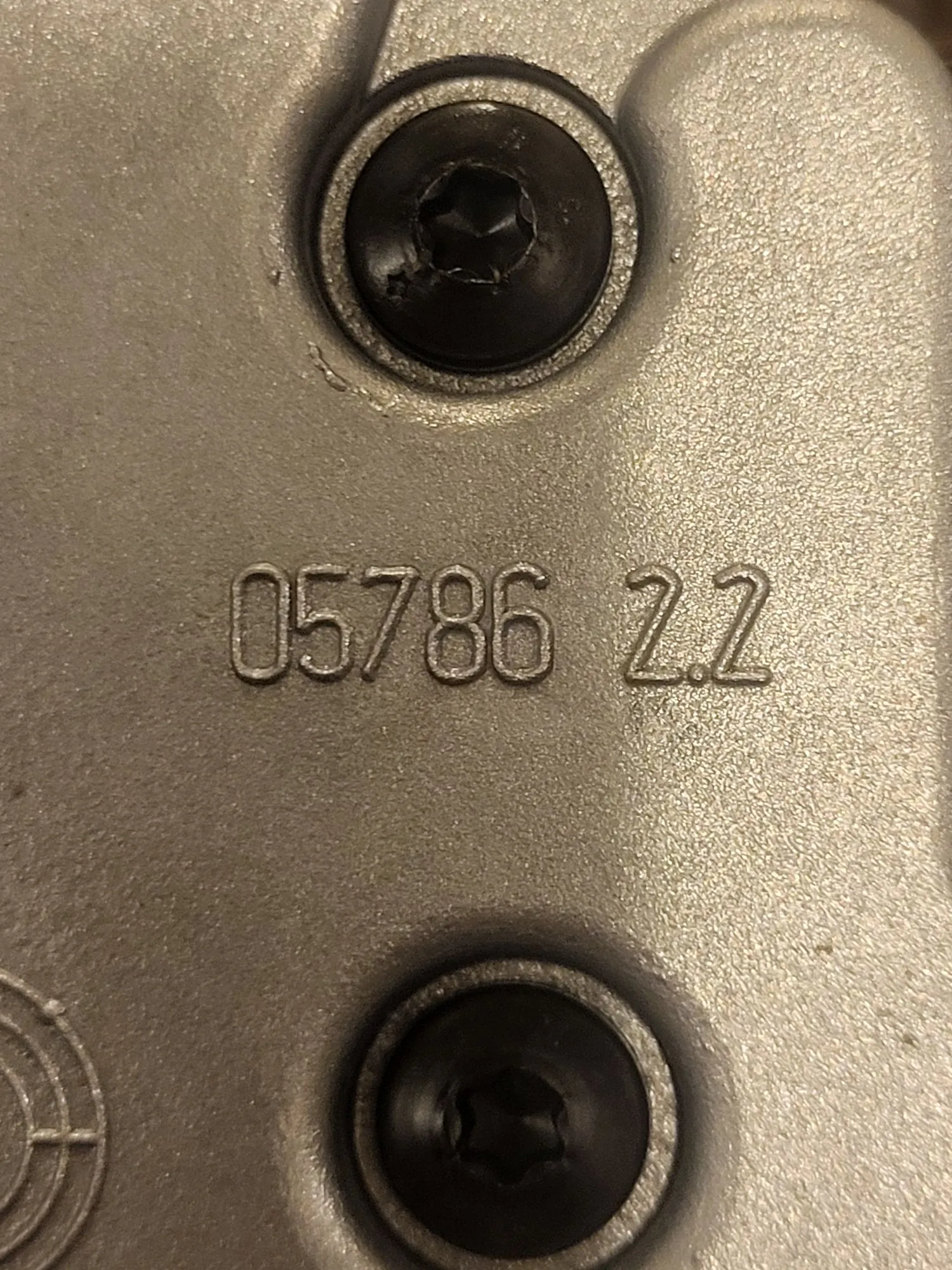 Zbliżenie na srebrną, metalową powierzchnię z dwiema czarnymi śrubami z łbem imbusowym, jedną u góry i jedną na dole. Pomiędzy śrubami znajduje się wytłoczony numer: 05786 2.2