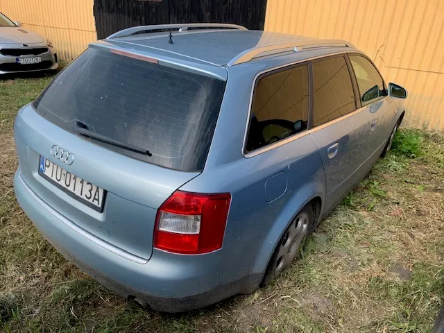 Niebieski samochód marki Audi w nadwoziu kombi, zaparkowany na trawie. Widoczny jest tył i prawy bok pojazdu. Samochód ma polską tablicę rejestracyjną o numerze PIU 0113A. Na dachu znajdują się srebrne relingi. W tle widoczny jest fragment innego, białego samochodu oraz żółta ściana budynku.
