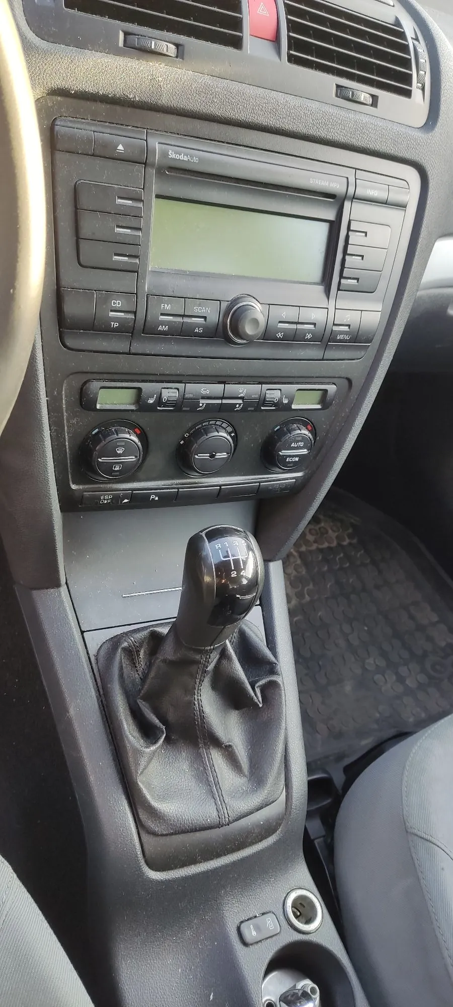Wnętrze samochodu marki Škoda, widok na konsolę środkową. Na górze znajduje się radio z napisem 'Škoda auto' i 'STREAM MP3', poniżej panel sterowania klimatyzacją z trzema pokrętłami i przyciskami 'AUTO' oraz 'ECON'. W dolnej części widoczna jest dźwignia zmiany biegów w skórzanej osłonie oraz uchwyty na kubki.