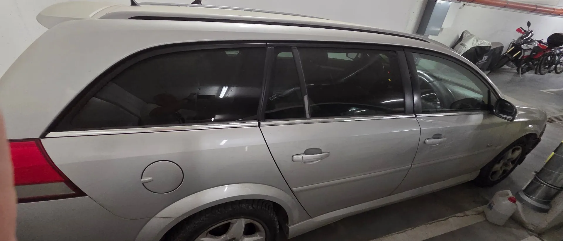 Boczny widok srebrnego samochodu typu kombi zaparkowanego w garażu. Widoczne są drzwi pasażera, tylne szyby oraz wlew paliwa.