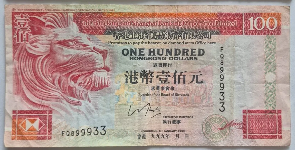 Banknot o nominale 100 dolarów Hongkongu wydany przez The Hongkong and Shanghai Banking Corporation Limited. Po lewej stronie znajduje się czerwony profil głowy lwa. W centralnej części widnieje napis 'ONE HUNDRED HONGKONG DOLLARS' oraz odpowiadające mu znaki chińskie. Na banknocie widnieje numer seryjny F0899933, podpisy dyrektorów oraz data '1st JANUARY 1990'. Dominujące kolory to czerwony, różowy i beżowy.