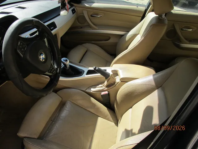 Wnętrze samochodu marki BMW z beżową skórzaną tapicerką. Widoczna jest kierownica z logo BMW, przednie fotele, konsola środkowa z lewarkiem zmiany biegów oraz hamulcem ręcznym. W prawym dolnym rogu znajduje się pomarańczowy napis z datą 08/09/2026.