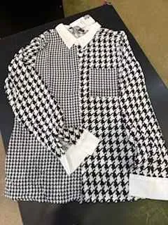 Czarno-biała odzież w klasyczny wzór houndstooth z trzema białymi etykietami, ułożona na ciemnej powierzchni. W tle fragment jasnej ściany lub podłoża.