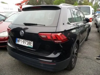 Czarny samochód osobowy marki Volkswagen typu SUV widziany od tyłu. Na tylnej szybie widoczny wycieraczka, a na bagażniku logo marki. Tablica rejestracyjna z białym tłem i czarnym napisem WP 49738E. W tle inne zaparkowane pojazdy, w tym czerwony i biały samochód, oraz fragmenty drzew i budynków. Samochód stoi na asfaltowym parkingu.