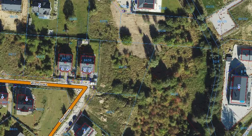 Zdjęcie satelitarne terenu z naniesionymi niebieskimi i czerwonymi liniami granic działek oraz numeracją. Widoczne są domy jednorodzinne, obszary zalesione i trawniki. Przez obraz przebiega droga oznaczona nazwą „Wierzbowa”. Na działkach widoczne są czerwone ramki z numerami takimi jak 84/57, 84/58, 60/95.