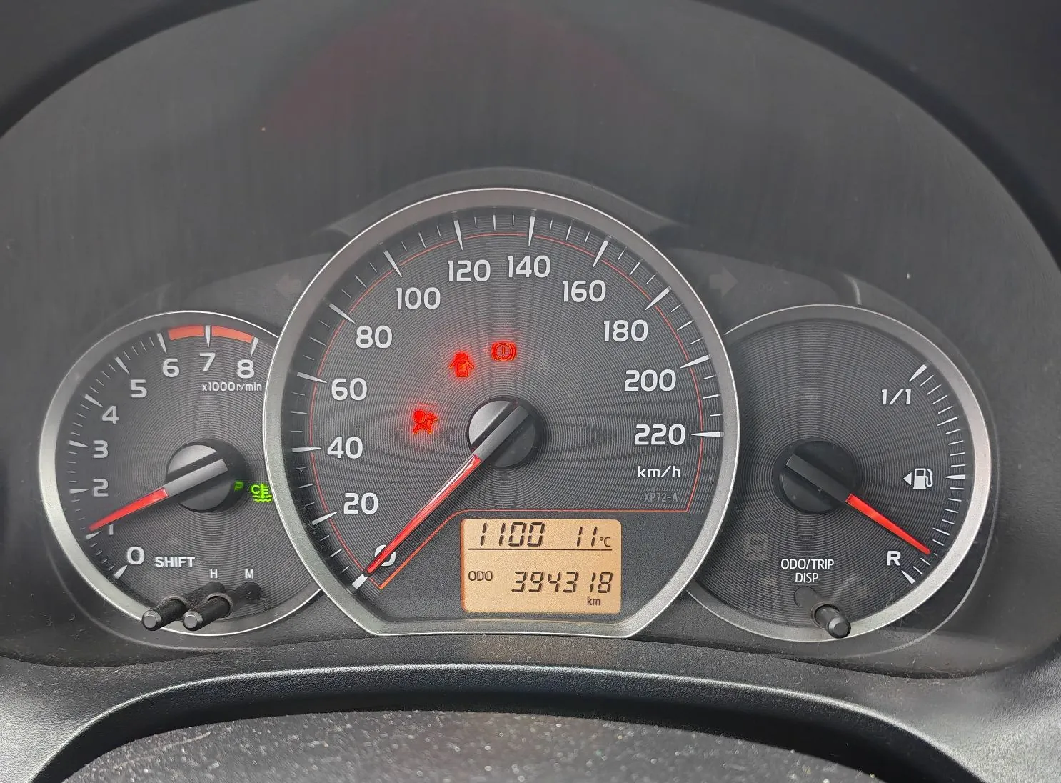 Panel instrumentów w samochodzie. Po lewej znajduje się obrotomierz z oznaczeniami od 0 do 8 x1000r/min. W centrum znajduje się prędkościomierz z zakresem do 220 km/h, na którym widnieje czerwona kontrolka układu hamulcowego. Poniżej prędkościomierza znajduje się cyfrowy wyświetlacz pokazujący godzinę 11:00, temperaturę 11°C oraz przebieg ODO 394318 km. Po prawej stronie znajduje się wskaźnik poziomu paliwa z oznaczeniem 1/1.