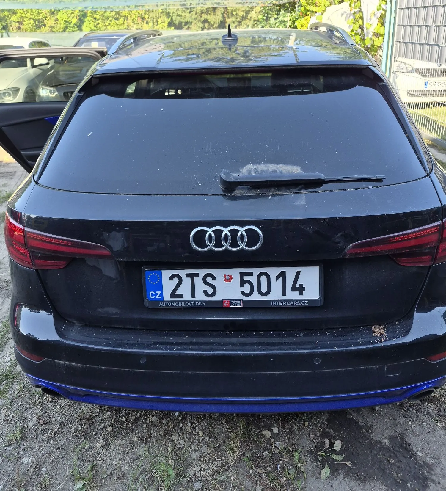 Tylny widok czarnego samochodu marki Audi. Na klapie bagażnika znajduje się logo Audi oraz czeska tablica rejestracyjna o numerze 2TS 5014. Poniżej tablicy widnieją napisy 'AUTOMOBILOVE DILY' oraz 'INTERCARS.CZ'. Samochód ma niebieski element wykończenia dolnej części zderzaka.