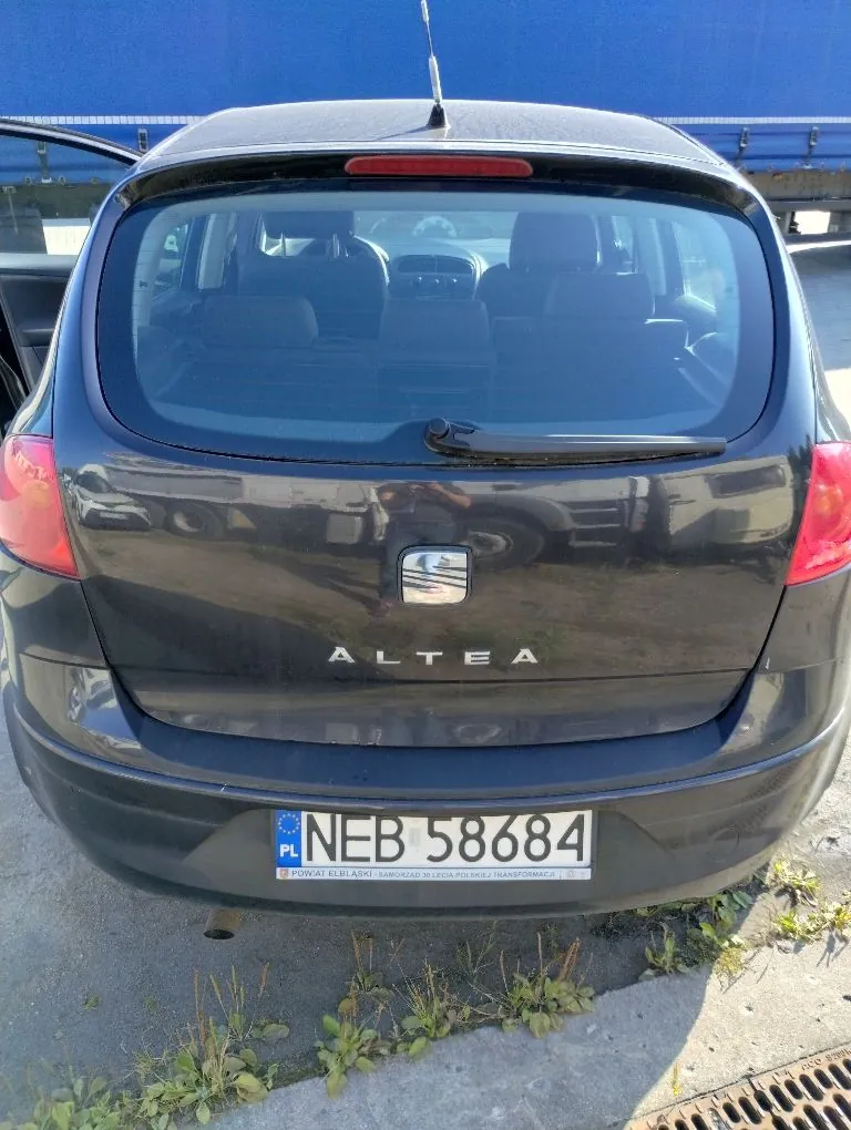 Tylny widok ciemnoszarego samochodu marki Seat Altea. Na klapie bagażnika znajduje się logo marki oraz napis 'ALTEA'. Samochód posiada polską tablicę rejestracyjną o numerze NEB 58684, pod którą widnieje napis 'POWIAT ELBLĄSKI SAMORZĄD ZIELONA POLSKA / TRANSFORMACJA'.