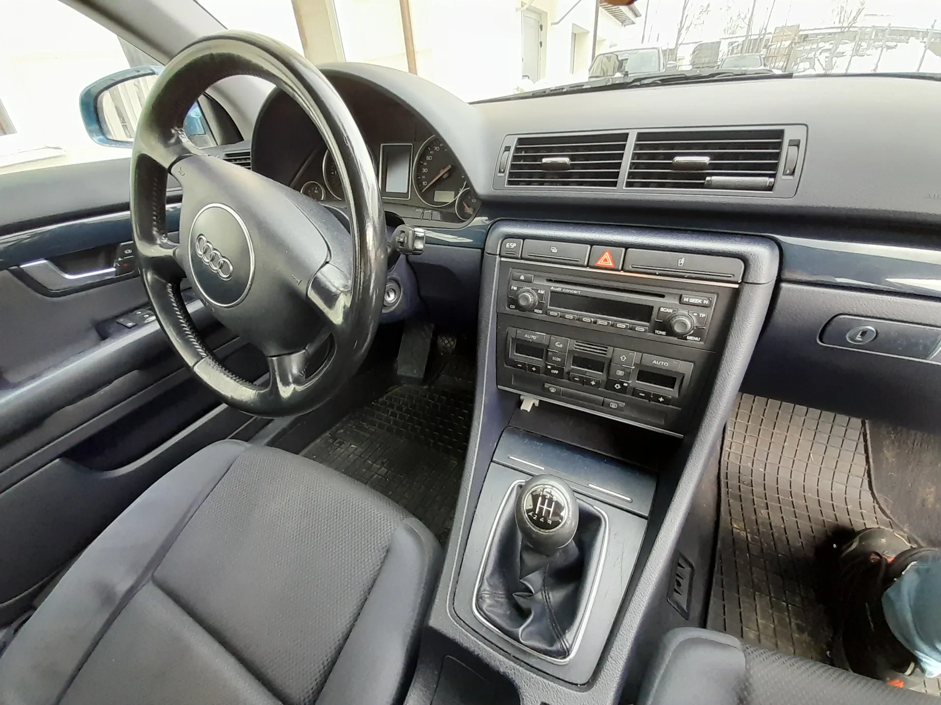 Kierownica z logo Audi, deska rozdzielcza z licznikami, klimatyzacją i radiem z napisem „Audi concert”. Ręczna skrzynia biegów, szare siedzenia, czarne maty podłogowe. Widoczne przyciski: „AUTO”, „SCAN”, „TP” oraz czerwony przycisk awaryjny.