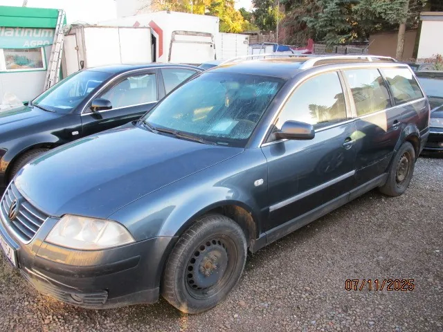 Ciemnoniebieski samochód typu kombi zaparkowany na żwirowym placu. W tle widoczne są inne pojazdy, budynek z zielonym napisem "Platinum" oraz drzewa. W prawym dolnym rogu obrazu znajduje się data "07/11/2025". Samochód ma czarne felgi i dachowy bagażnik. W tle również białe kontenery i fragmenty innych budynków.