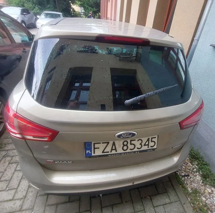 Tylny widok beżowego samochodu marki Ford. Na klapie bagażnika znajduje się logo Ford oraz tablica rejestracyjna o numerze FZA 85345 z oznaczeniem PL. Poniżej tablicy widnieje napis wendt-mobile.de. Samochód zaparkowany jest na kostce brukowej.