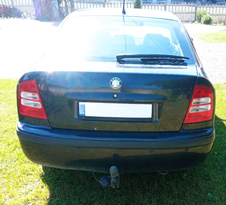 Tylny widok czarnego samochodu marki Skoda zaparkowanego na trawie. Widoczny jest hak holowniczy, tylna szyba z wycieraczką oraz biała tablica rejestracyjna, która została zamazana.