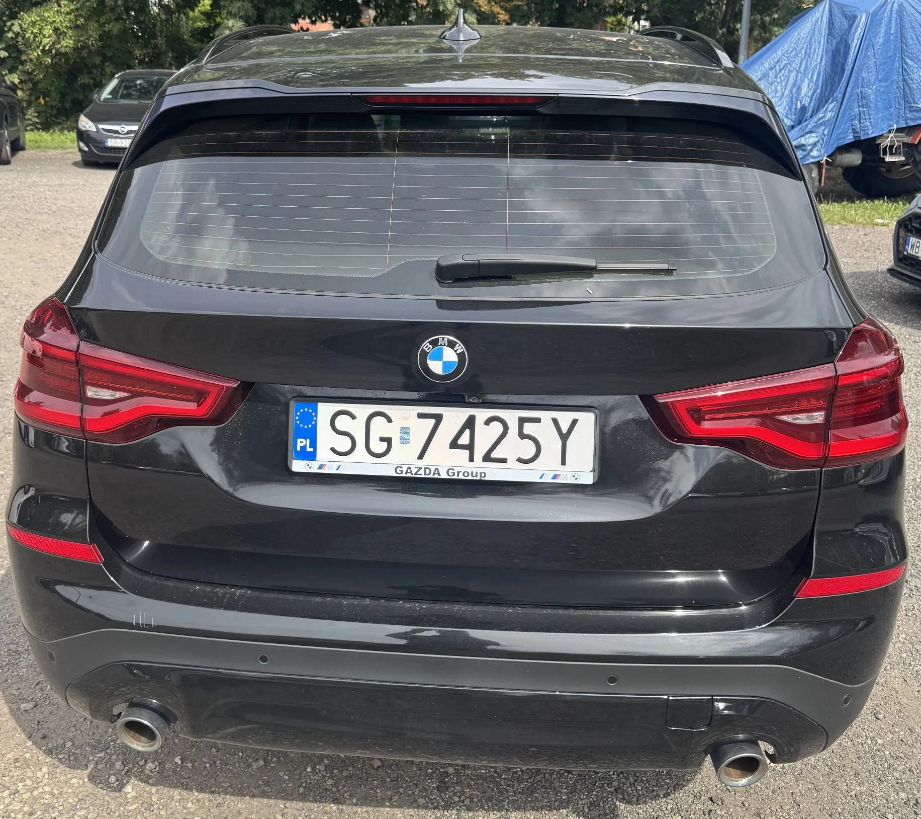 Tylny widok czarnego samochodu marki BMW. Na klapie bagażnika znajduje się logo BMW oraz polska tablica rejestracyjna o numerze SG 7425Y z napisem GAZDA Group na ramce. Samochód ma dwa rury wydechowe po obu stronach dolnego zderzaka.