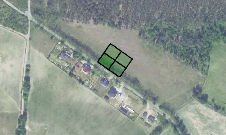 Zdjęcie satelitarne terenu z zabudowaniami i zielenią. Na obrazie widoczna jest grupa domów z oznaczeniami tekstowymi: '2B', '2C', '2D' oraz '2E'. W centralnej części znajduje się czarny kwadrat podzielony na cztery mniejsze pola, z których lewe górne jest wypełnione kolorem zielonym.