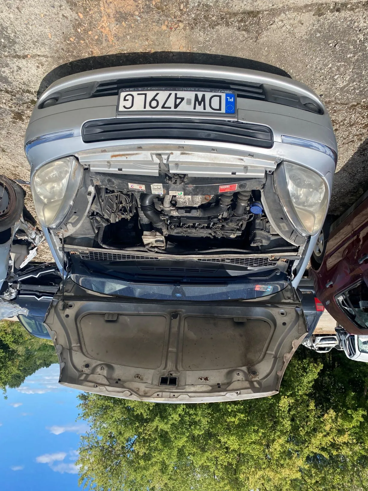 Srebrny samochód z otwartą maską, ukazujący silnik. Pojazd posiada tablicę rejestracyjną o numerze DW 479LG. Zdjęcie jest zorientowane poziomo, podczas gdy samochód stoi pionowo.