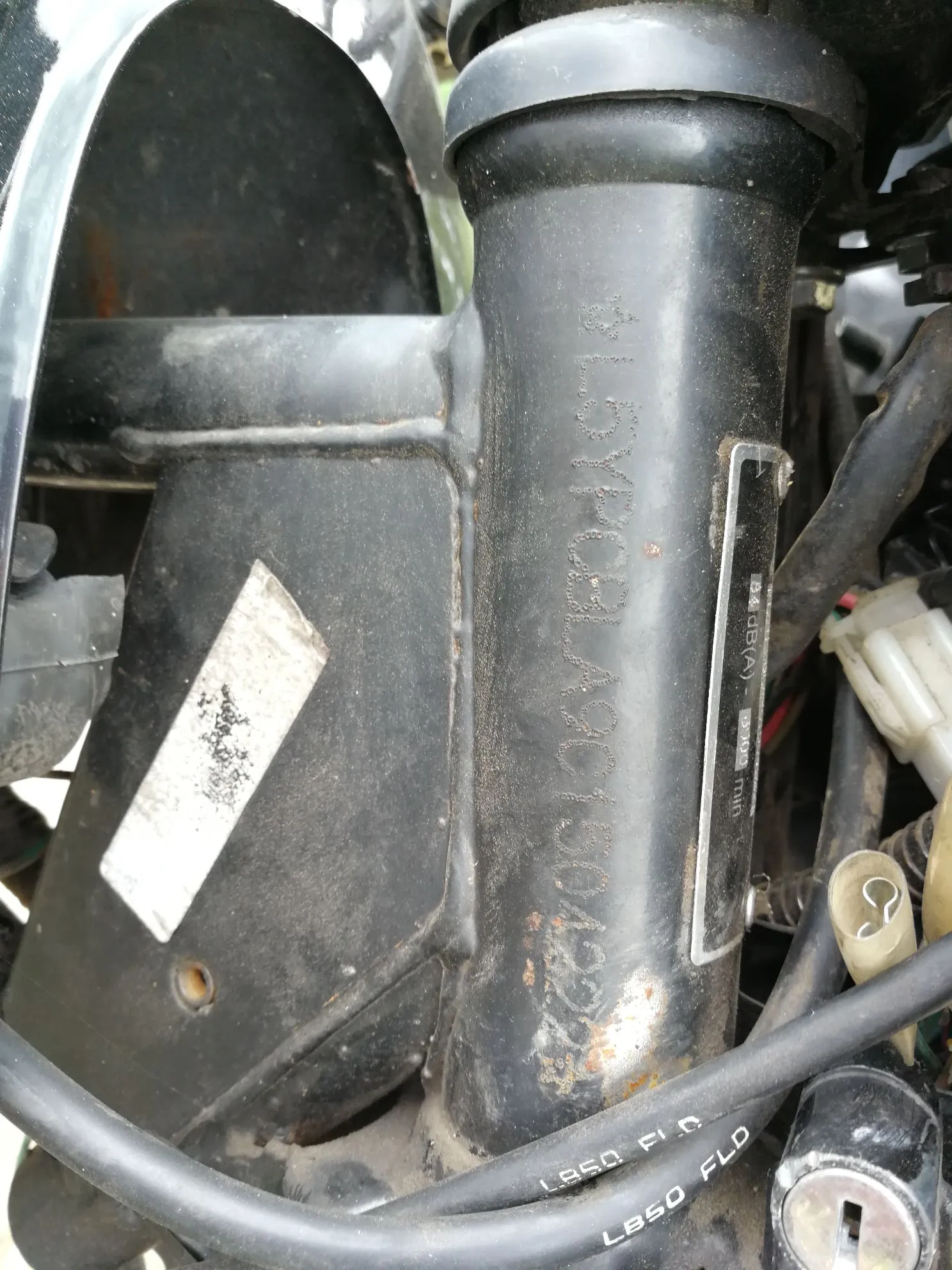Zbliżenie na czarne, metalowe elementy ramy motocykla. Na pionowej rurze znajduje się wybity numer VIN: L5YPCB LA90113042222. Obok numeru widoczna jest mała, srebrna tabliczka znamionowa z tekstem „89 dB(A)” oraz „2000 min”. W dolnej części obrazu widoczny jest czarny przewód z białym napisem „LB50 FLD”.