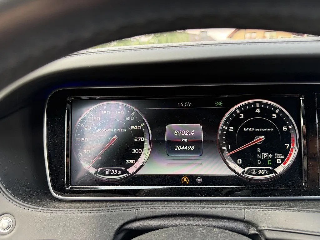 Widok z wnętrza samochodu na cyfrowy zestaw wskaźników. Po lewej stronie znajduje się prędkościomierz z maksymalną wartością 330 km/h i logo AMG. Po prawej stronie znajduje się obrotomierz z oznaczeniem V8 BITURBO. W centralnej części ekranu widnieją liczby: 8902.4 km oraz 204498. Na górze wyświetlona jest temperatura 16.5°C. Na dole widoczne są wskaźniki temperatury oleju (90°C) oraz poziomu paliwa (35%).