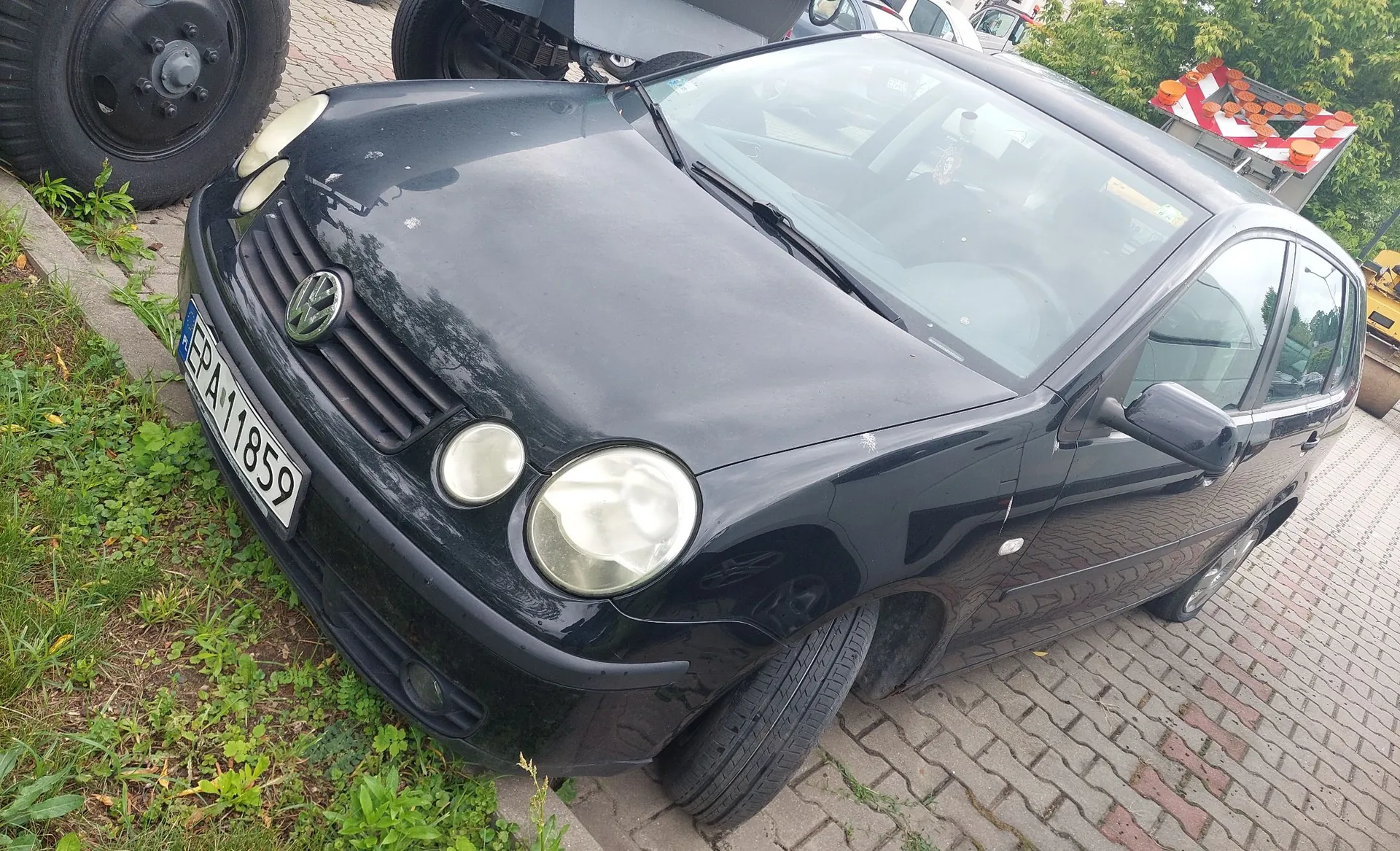 Czarny samochód marki Volkswagen Golf IV zaparkowany na kostce brukowej. Widoczny jest przód pojazdu z tablicą rejestracyjną o numerze EPA 11859. Samochód stoi częściowo na trawie.