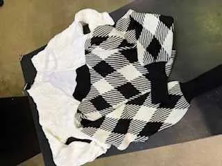 Czarno-biały sweter w argyle z białą koszulą pod spodem leżące na ciemnej powierzchni. Tło składa się z częściowo widocznej zielonkawej powierzchni i ciemnego obszaru. Sweter ma charakterystyczny wzór rombów z czarnymi i białymi pasami.