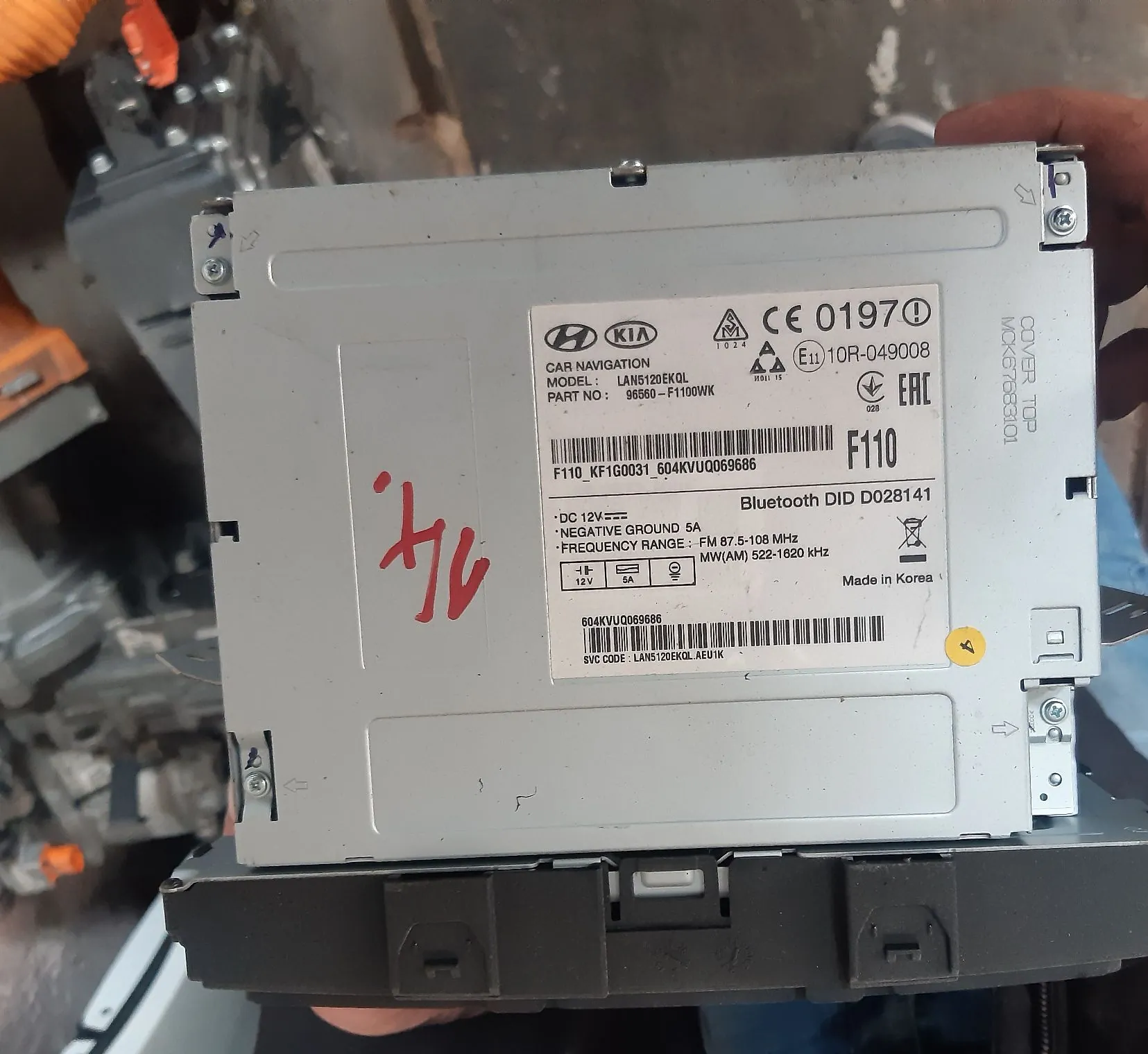 Zdjęcie tylnej obudowy srebrnego urządzenia elektronicznego, prawdopodobnie radia samochodowego. Na białej naklejce widoczne są logotypy Hyundai i KIA oraz napis 'CAR NAVIGATION'. Tekst na naklejce zawiera informacje: 'MODEL: LAN6121EKQL', 'PART NO: 96568-F110WK', 'F110 KF1G0031 504KVUQ069686', 'Bluetooth DID D028141', 'DC 12V', 'NEGATIVE GROUND 5A', 'FREQUENCY RANGE: FM 87.5-108 MHz, MW(AM) 522-1620 kHz' oraz 'Made in Korea'. Na obudowie znajduje się czerwony odręczny napis '4/6'.