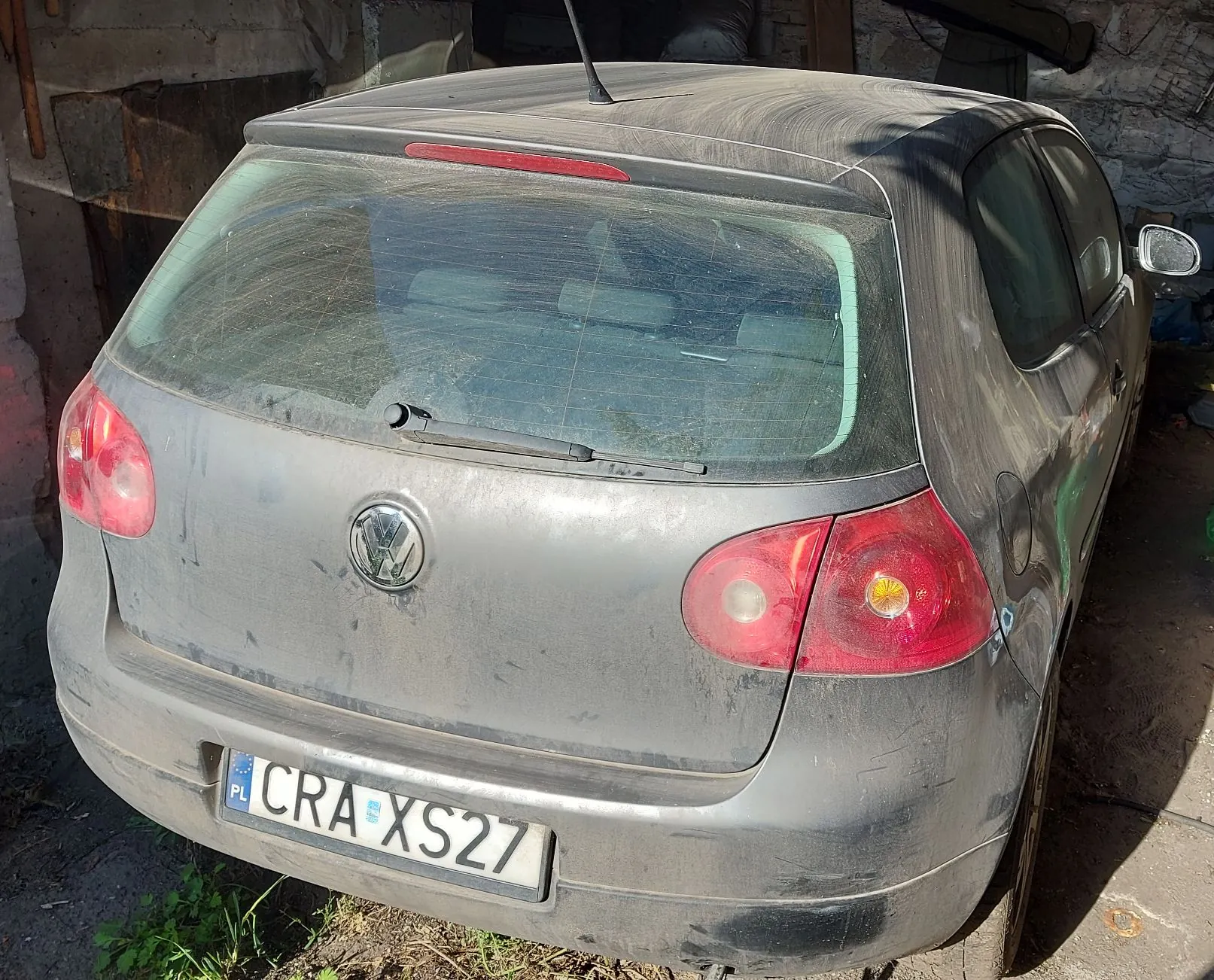 Tylny widok zakurzonego, szarego samochodu marki Volkswagen Golf. Pojazd posiada polską tablicę rejestracyjną o numerze CRA XS27. Samochód stoi w garażu lub pomieszczeniu gospodarczym.