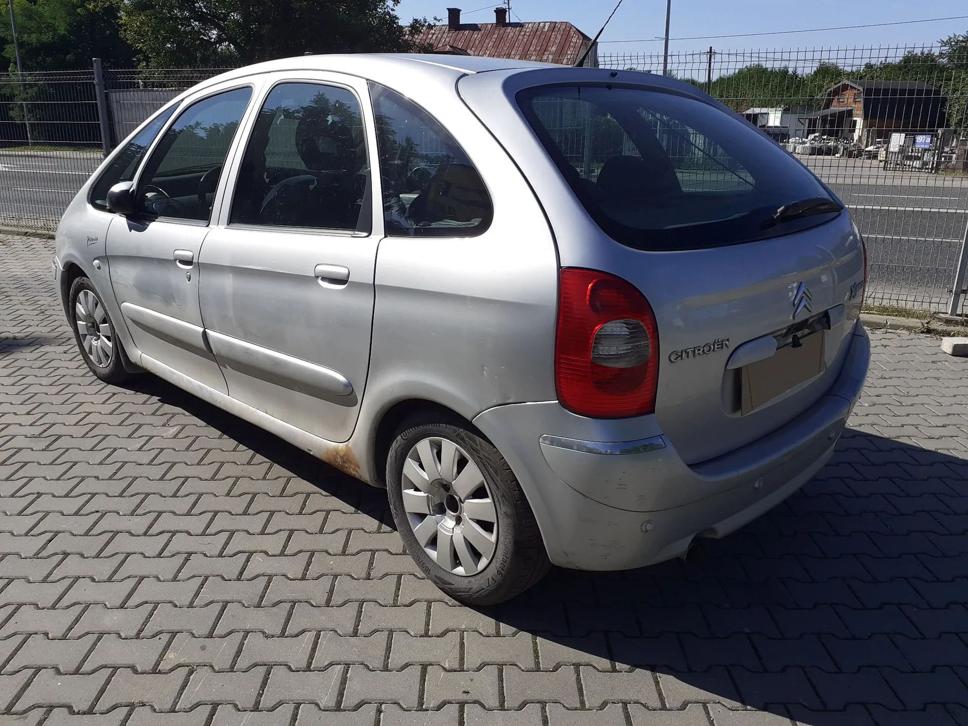 Srebrny samochód osobowy marki Citroën w nadwoziu hatchback, zaparkowany na kostce brukowej. Pojazd jest widoczny z tyłu i z boku. Na klapie bagażnika znajduje się logo marki oraz napis CITROËN.