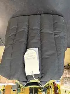 Czarna pikowana kamizelka leżąca na ciemnej powierzchni. Na kamizelce widoczna biała etykieta z napisem '100% POLYESTER'. W tle rozmyty widok wnętrza sklepu z półkami i przedmiotami.