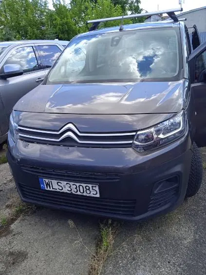 Szary samochód marki Citroën z zamontowanym bagażnikiem dachowym, zaparkowany obok innego srebrnego auta. Na przodzie pojazdu widoczna jest tablica rejestracyjna o numerze WLS 33085.
