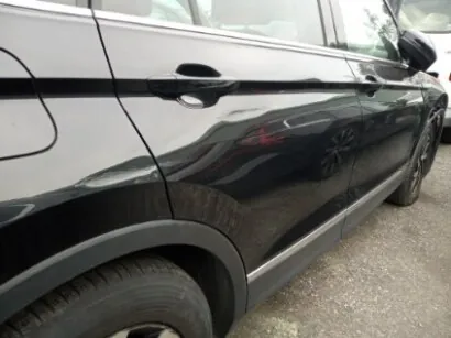 Czarny samochód typu SUV widziany z boku, z widocznymi drzwiami, klamkami, kołami i lusterkami bocznymi. Na błyszczącej karoserii odbija się inny pojazd. Samochód stoi na podłożu z drobnej kostki. Brak czytelnego tekstu.