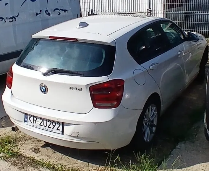 Biały samochód marki BMW w nadwoziu kombi, zaparkowany tyłem do obiektywu. Na klapie bagażnika widoczne jest logo BMW oraz oznaczenie modelu 120. Samochód posiada polską tablicę rejestracyjną o numerze KR 2U292.
