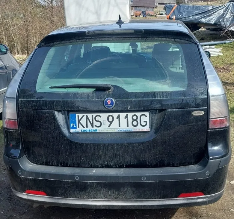 Tylny widok czarnego samochodu typu kombi. Pojazd jest zabrudzony pyłem i błotem. Na klapie bagażnika znajduje się polska tablica rejestracyjna o numerze KNS 9118G, a pod nią niebieski pasek z napisem LOGISCAR oraz numerem telefonu 533-888-456. Nad tablicą widoczne jest logo marki samochodu.