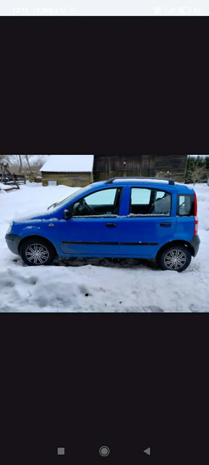 Niebieski samochód osobowy zaparkowany na śnieżnej powierzchni. Pojazd ma czarne akcenty i dachowy bagażnik. W tle drewniana chata z dachem pokrytym śniegiem oraz drzewa. Śnieg pokrywa również przednią szybę i dach samochodu. Na pierwszym planie widoczne są zaspy śnieżne.