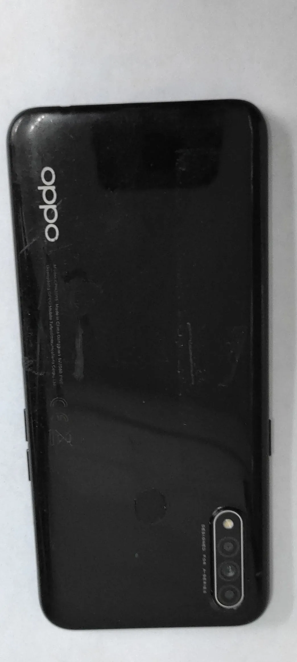 Czarny smartfon marki Oppo leżący poziomo na białym tle. Widoczny jest tył urządzenia z logo 'oppo' w prawym górnym rogu oraz modułem trzech aparatów fotograficznych i lampą błyskową w lewym dolnym rogu. Obok aparatów znajduje się napis 'DESIGNED FOR A-SERIES'.