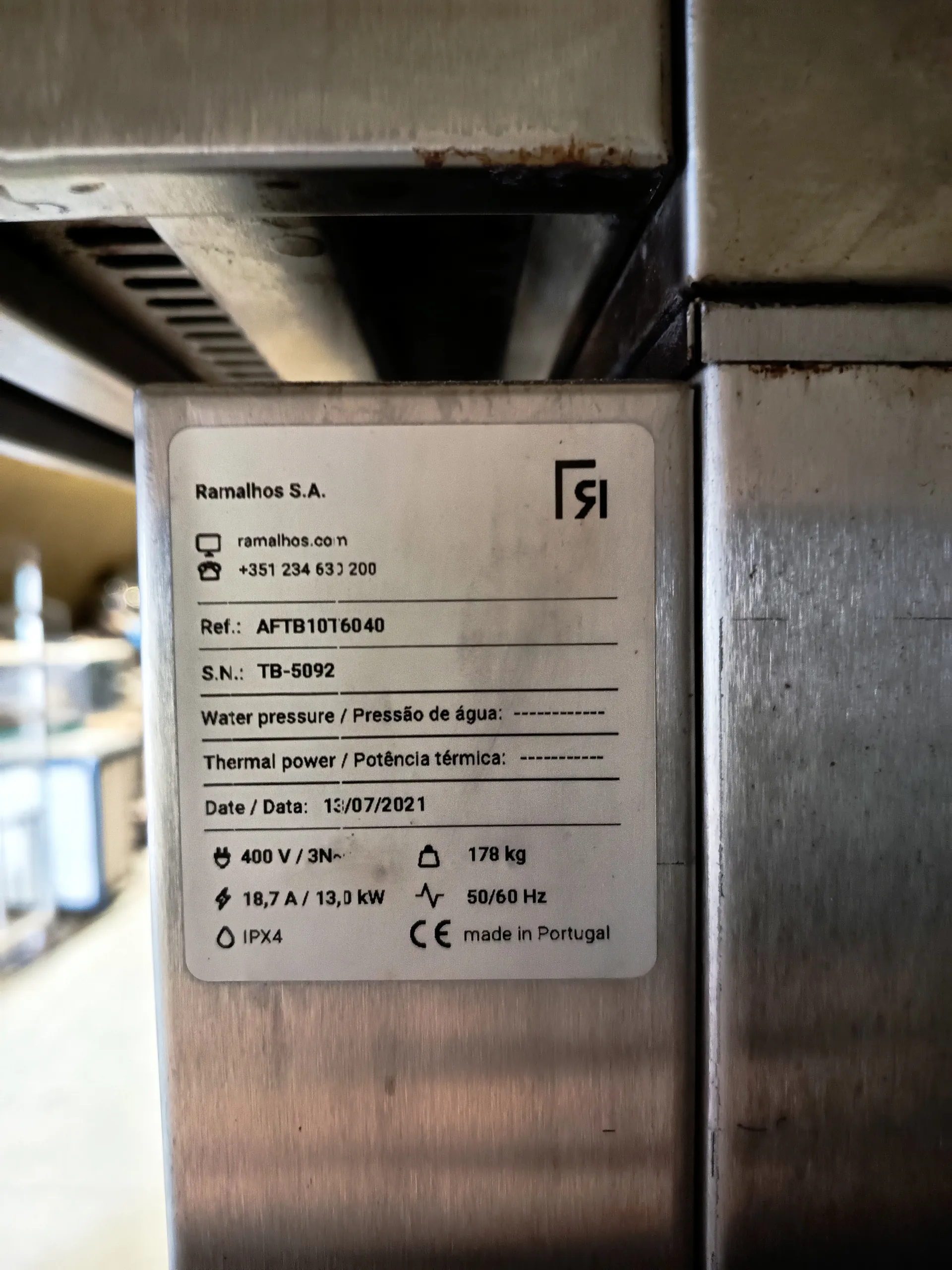 Tabliczka znamionowa firmy Ramalhos S.A. z danymi technicznymi: strona internetowa ramalhos.com, numer telefonu +351 234 631 200, numer referencyjny AFTB10T6040, numer seryjny TB-5092, ciśnienie wody / Pressão de água: ----------, moc termiczna / Potência térmica: ----------, data 13/07/2021, parametry elektryczne 400 V / 3N~, 18,7 A / 13,0 kW, 50/60 Hz, masa 178 kg, stopień ochrony IPX4, znak CE oraz napis 'made in Portugal'. Tabliczka zamontowana na metalowej powierzchni.