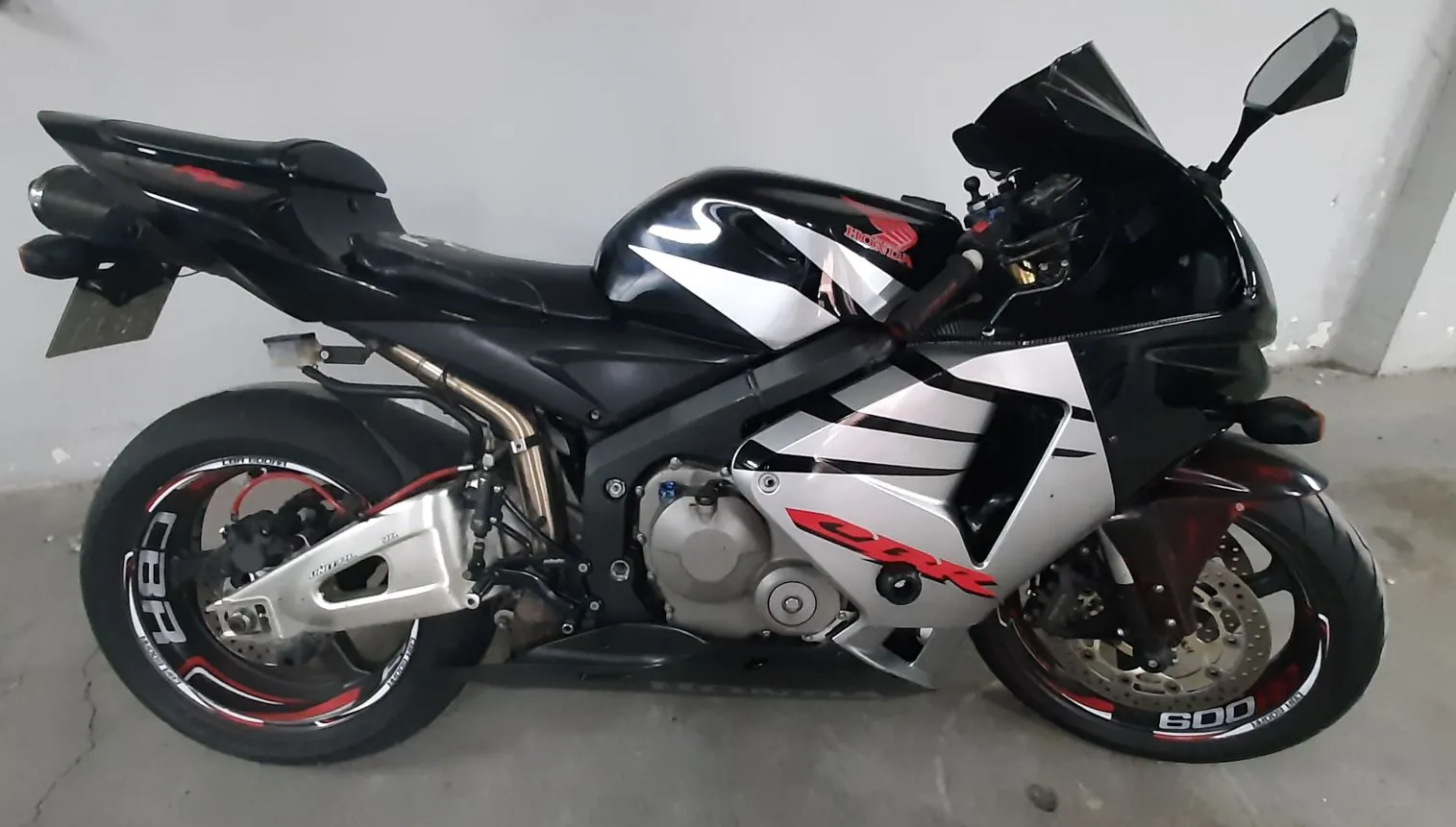 Czarny motocykl sportowy marki Honda CBR z białymi i czerwonymi akcentami graficznymi na owiewkach i felgach. Motocykl jest ustawiony bokiem na jasnym tle. Na boku owiewki widnieje czerwony napis 'CBR', a na przedniej oponie biały napis '600'.