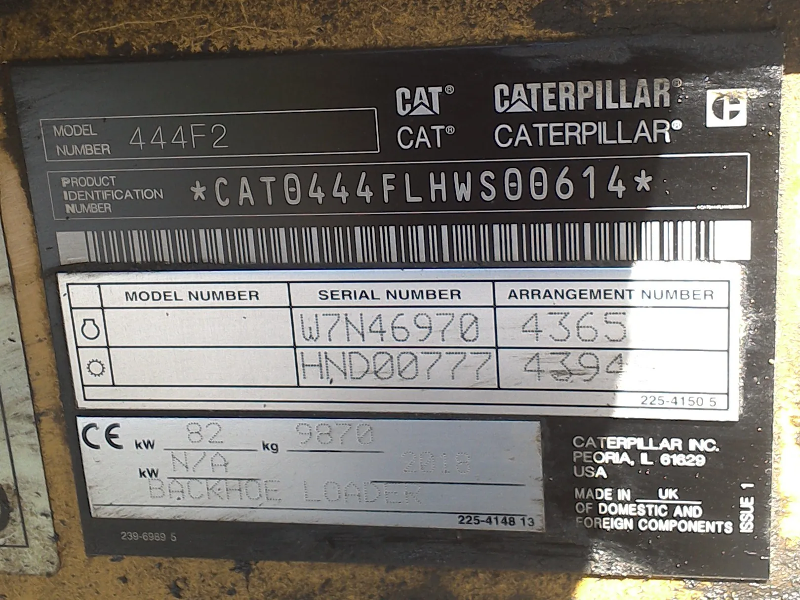 Czarna tabliczka znamionowa maszyny marki Caterpillar. Na górze widnieją logotypy CAT i napisy CATERPILLAR. Model Number: 444F2. Product Identification Number: *CAT0444FLHWS00614*. Poniżej znajduje się kod kreskowy. W tabeli widoczne są numery seryjne: W7N46970 (Arrangement Number 4365) oraz HND00777 (Arrangement Number 4394). W dolnej części znajduje się oznaczenie CE, dane techniczne: 82 kW, 9870 kg oraz napis BACKHOE LOADER. Producent: Caterpillar Inc., Peoria, IL 61629 USA, Made in UK of domestic and foreign components.